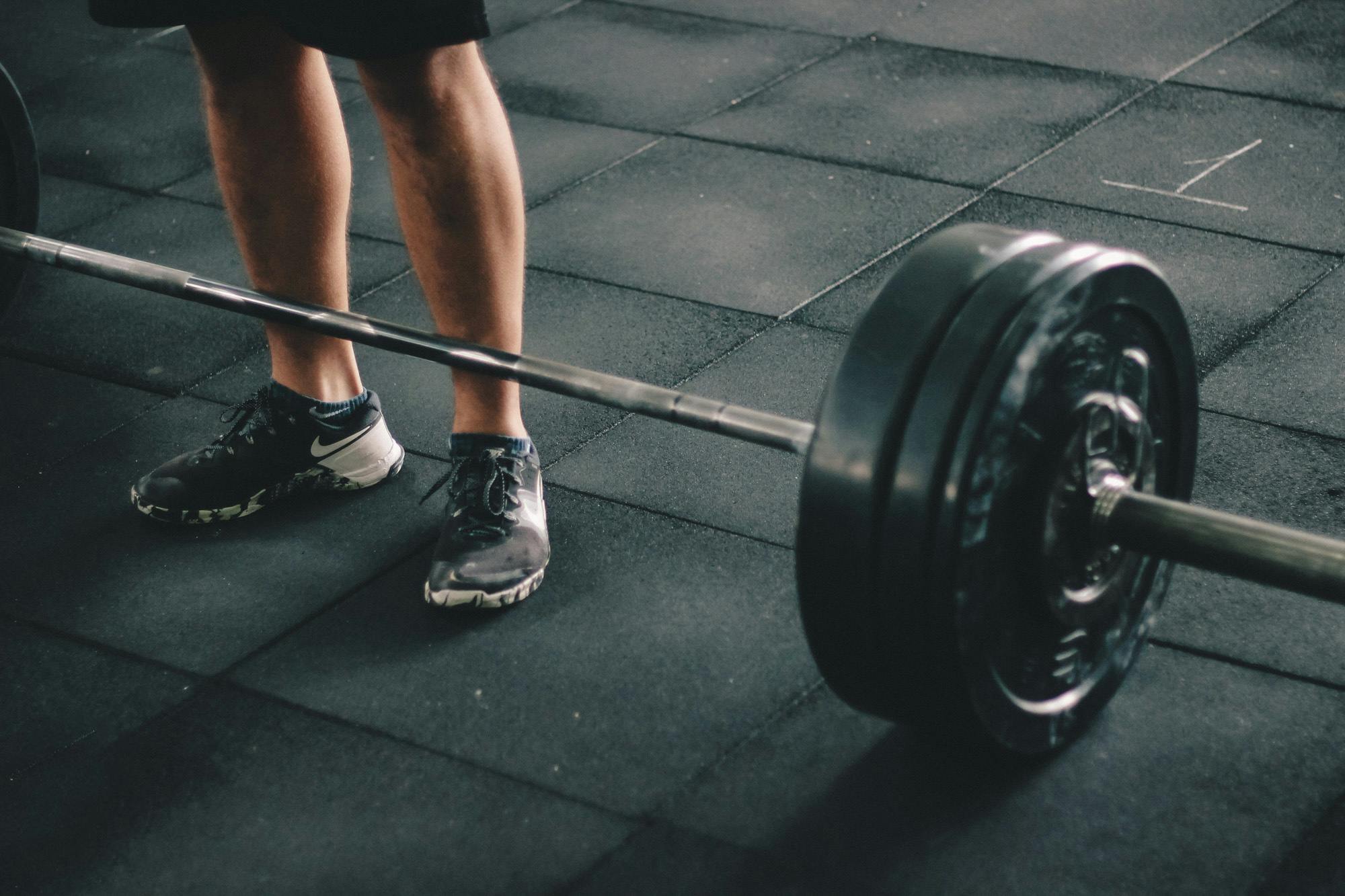 Etika Penggunaan Ruang Fitness Sudirman Suites Close-up of a man deadlifting a heavy barbell in an indoor gym setting.